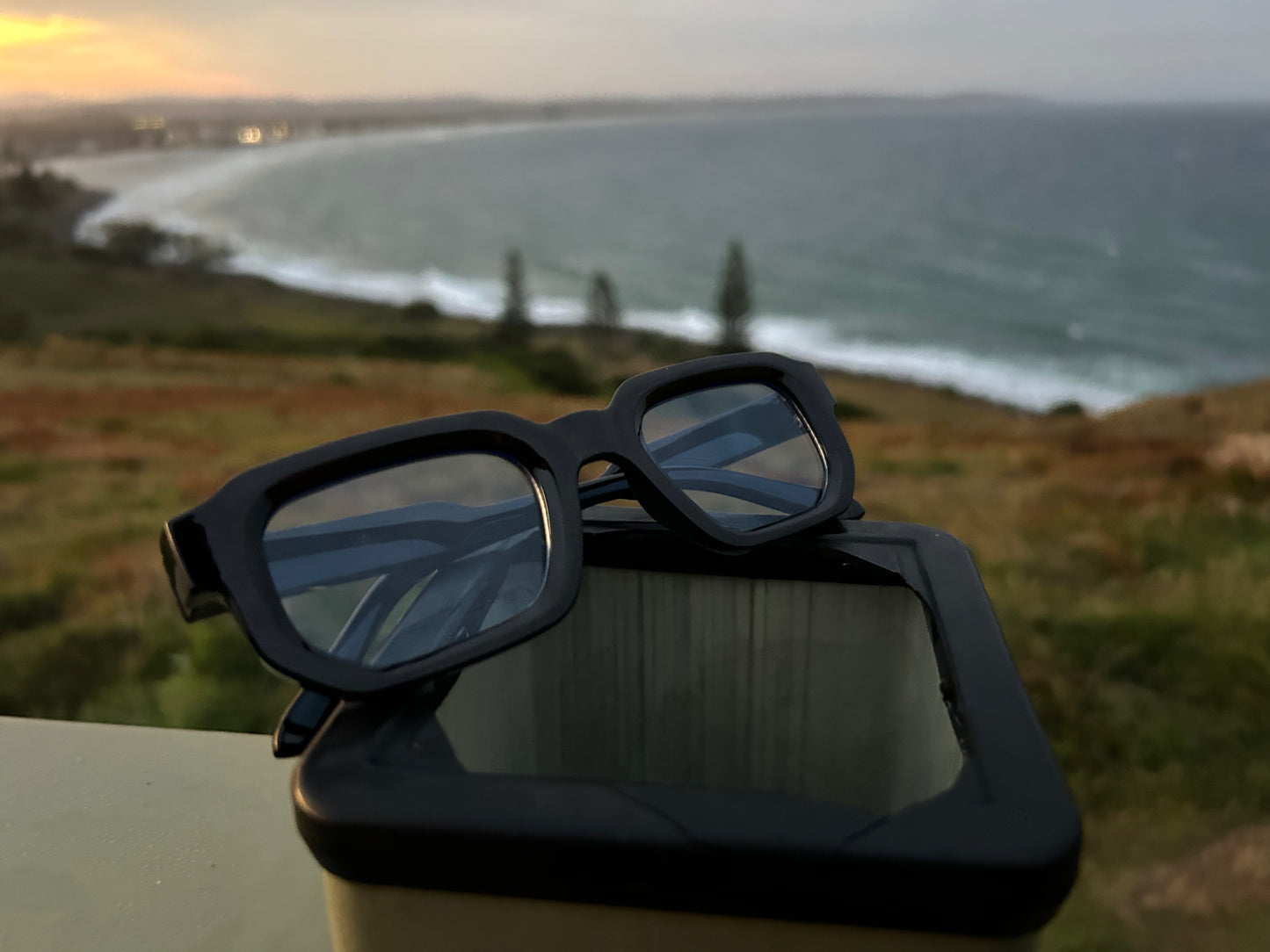 Black sunglasses on a car dashboard with a scenic ocean view in the background